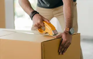 person taping shut a cardboard box